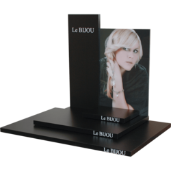 Thekendisplay 'Le BIJOU', bestehend aus einer Grundplatte, einer Sockelplatte und einem Podest, aus schwarzem Melaminspan mit Plakathalter aus Acrylglas